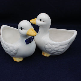 Two white ceramic duck-shaped bowls on a dark background