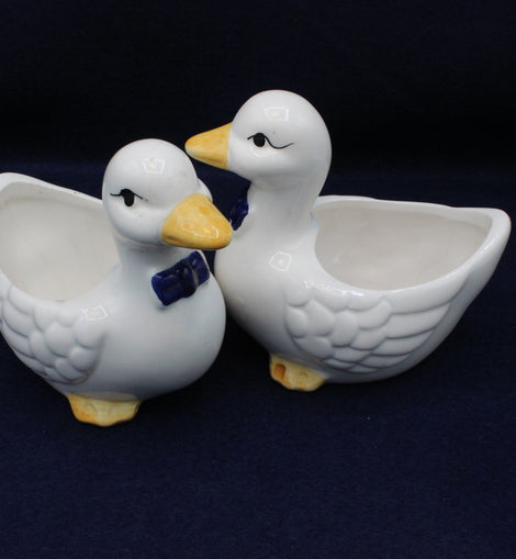 Two white ceramic duck-shaped bowls on a dark background