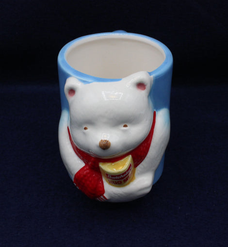 Ceramic mug shaped like a bear with a red scarf on a dark background