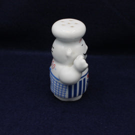 White ceramic saltshaker shaped like a chef with a blue apron on a dark background