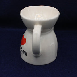 White ceramic tea pot with a red heart design on a dark blue background