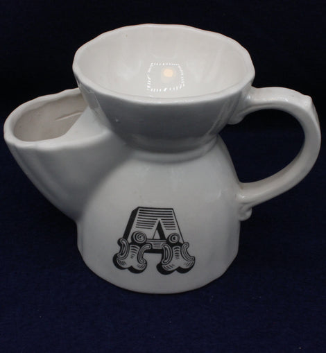 White ceramic tea pot with a handle and decorative letter 'A' on a dark background