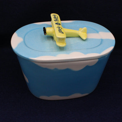 Blue container with white clouds and a yellow airplane on top against a black background