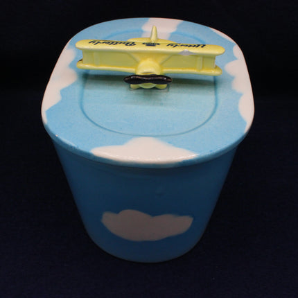 Blue container with white clouds and a yellow airplane on top against a black background