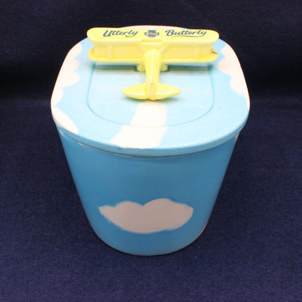 Blue container with a yellow lid featuring a butterfly design on a dark background