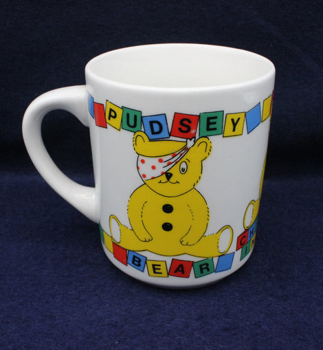 Pudsey Bear mug with a cartoon bear design and colorful text on a dark blue background
