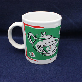 White mug with green and red design featuring a teapot on a blue background