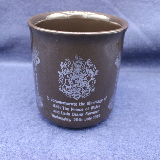 Brown ceramic cup with white text and emblem on a blue fabric background