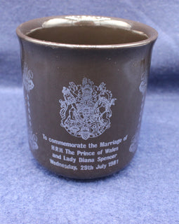 Brown ceramic cup with white text and emblem on a blue fabric background