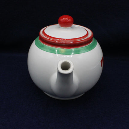White ceramic teapot with red and green accents on a black background