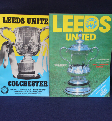 Two Leeds United football club match programs with trophies on a dark background