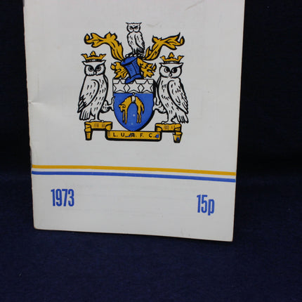 Small book or notebook with a crest design and year '1973' printed on it, against a dark background.