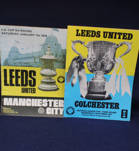 Two Leeds United football club matchday programmes from different matches on a dark background.
