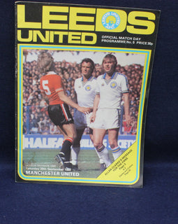 Leeds United football match day programme cover with players and text on a dark background