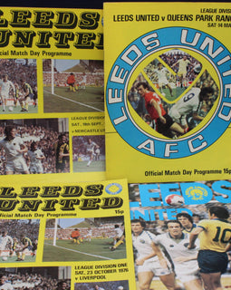 Three Leeds United football match day programmes from different years on a dark background.