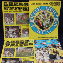 Three Leeds United football match day programmes from different years on a dark background.