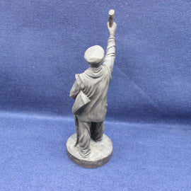 Statue of a person in a robe and hat holding a newspaper on a blue background