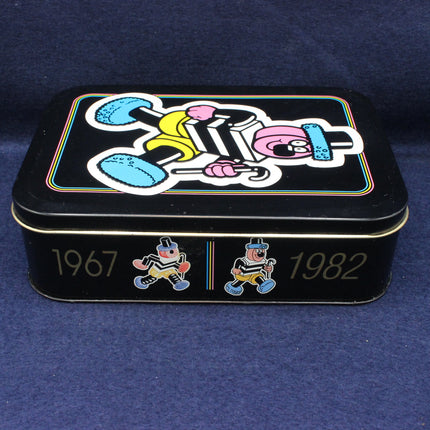 Black tin box with colorful graphics and years 1967 and 1982 on a blue background