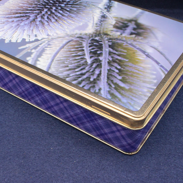 Close-up of a decorative glass plate with a gold rim and blue plaid pattern on a dark surface.
