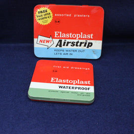 Two Elastoplast Airstrip packaging tins on a dark blue background