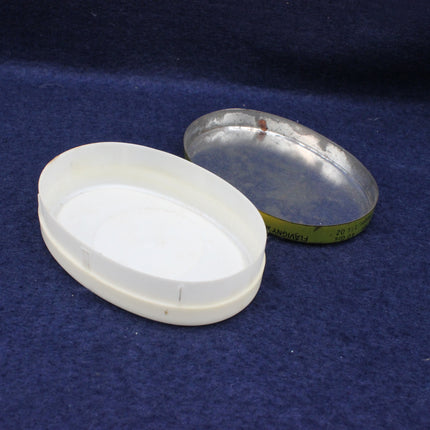 Two oval containers, one white and one metallic, on a blue textured surface.