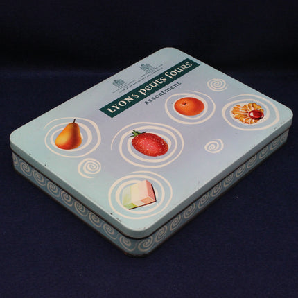 Tin box with fruit illustrations and 'Lyons petits fours' text on a dark background