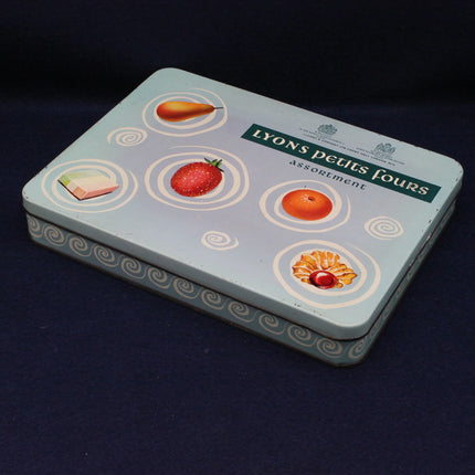 Tin box with illustrations of fruits and 'Lyons' branding on a dark background