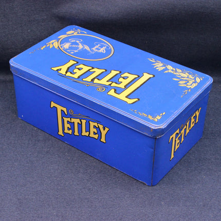 Blue Tetley tea tin with yellow text on a dark background