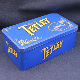Blue Tetley tea tin with gold text on a dark background