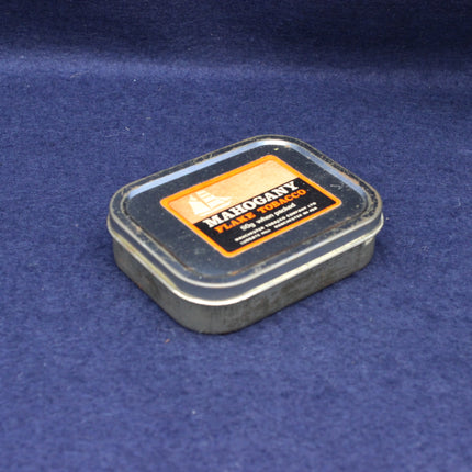 Small metal tin labeled 'Manogany Flake Tobacco' on a blue background