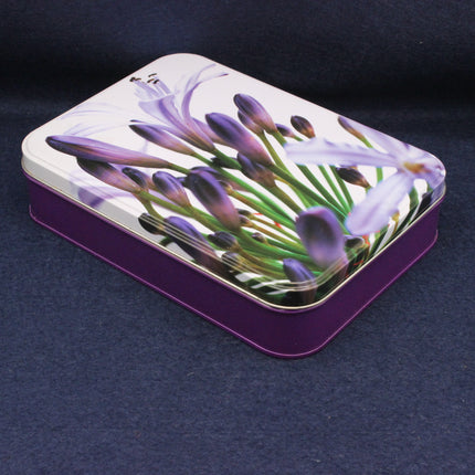 Tin box with purple flower design on a dark background