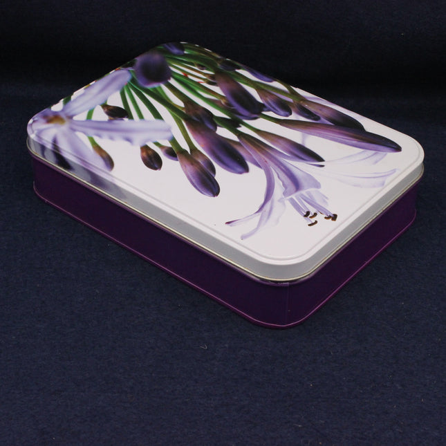 Tin box with purple floral design on a dark background