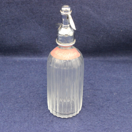Clear glass seltzer bottle with a silver top on a blue background