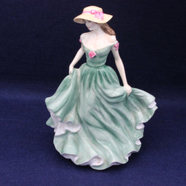 Porcelain figurine of a woman in a green dress with a pink hat on a dark blue background