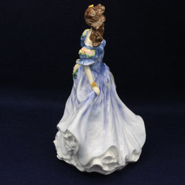 Porcelain figurine of a woman in a blue dress holding a parasol on a dark background