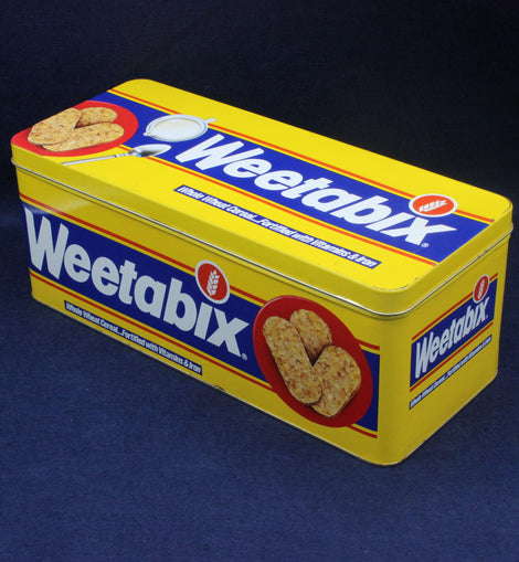Yellow Weetabix tin with blue and red accents on a dark background