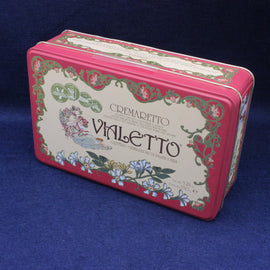 Decorative pink tin box with floral designs and 'Cremaretto Vialetto' text on a blue background