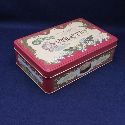 Decorative red tin box with floral designs and text on a blue background