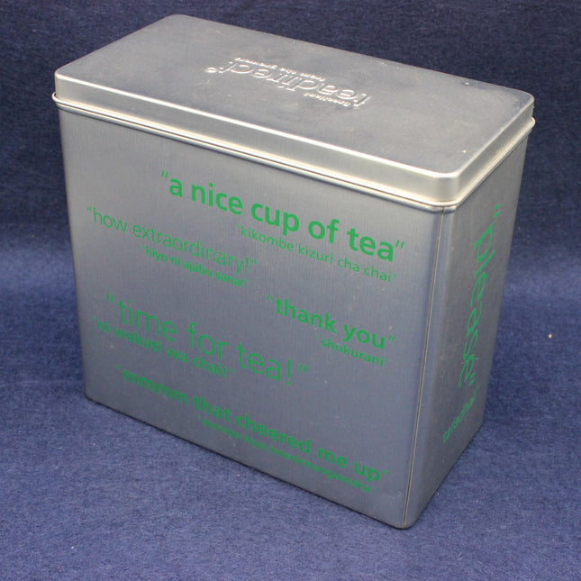 Gray tea tin with green multilingual text on a blue background