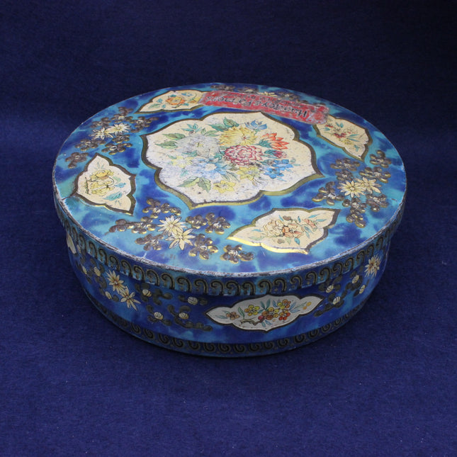 Decorative round biscuit tin with floral patterns on a blue background