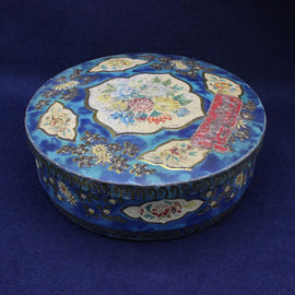 Decorative round biscuit tin with floral patterns on a blue background