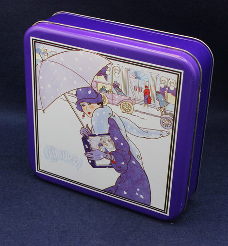 Tin box with a decorative design of a woman holding an umbrella on a snowy street.