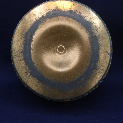 Round metallic tin with concentric circles on a dark background
