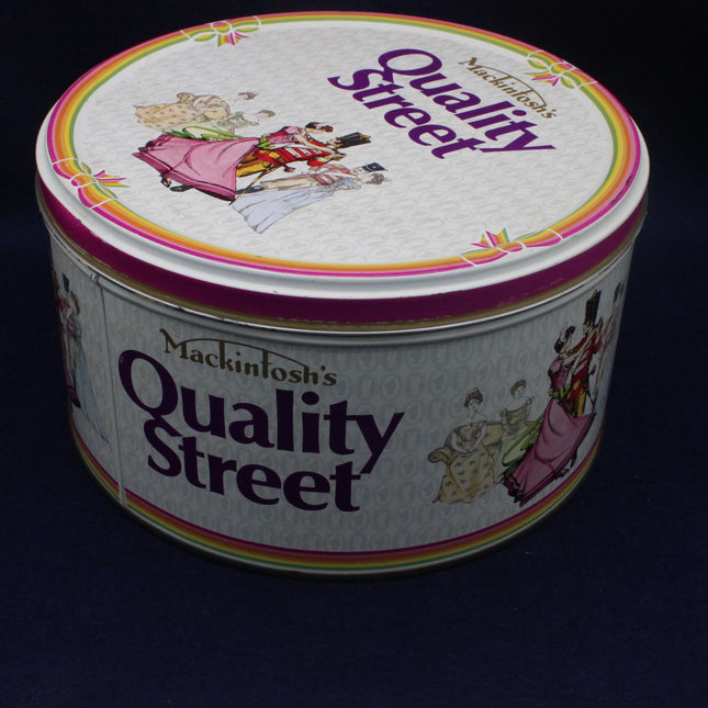 Round Quality Street tin with colorful label on a black background