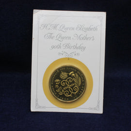 Gold coin on a card with text about Queen Elizabeth's Mothers 90th birthday, against a dark background.