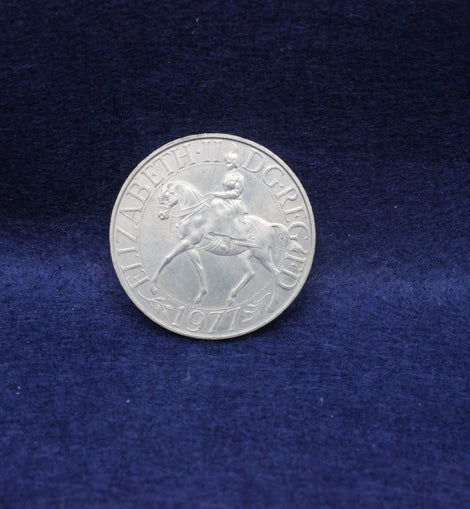 Silver Queen Elizabeth 1977 coin with the queen on a horse on a blue fabric background