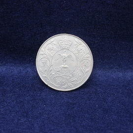 Silver 1977 Queen Elizabeth coin with intricate design on a blue fabric background