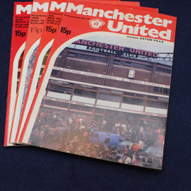 Stack of Manchester United football club programmes on a dark background