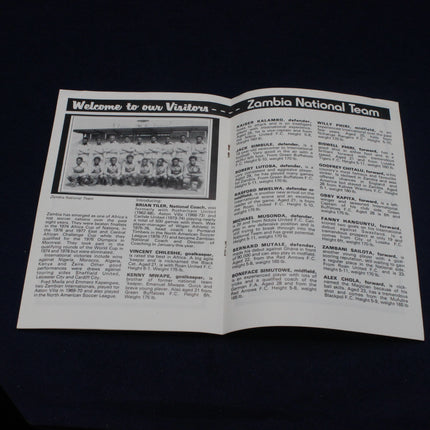 Open leaflet with text and black-and-white photo of a Zambia National Team on a dark background