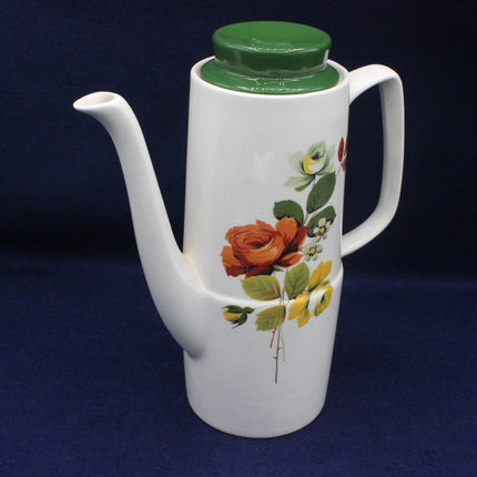 White ceramic teapot with floral design and green lid on a dark background